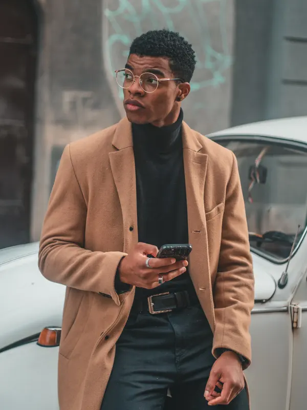 Mann mit Brille und camelfarbenem Mantel lehnt an einem Oldtimer